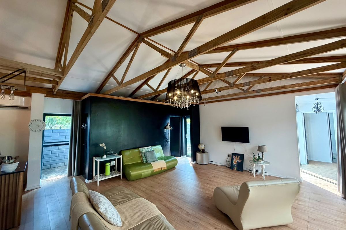 Spacious living room featuring a high vaulted ceiling with exposed timber trusses, laminate flooring, and a modern black feature wall.