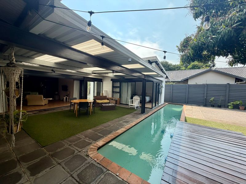 Outdoor entertainment area featuring a swimming pool, covered patio with steel beams, timber decking, and direct access to the interior living space.