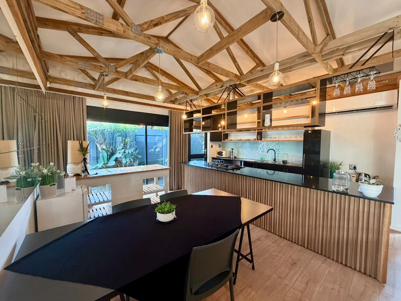 Spacious open-plan kitchen and dining area featuring exposed timber roof trusses, modern cabinetry, stone countertops, and large sliding doors leading to the garden.