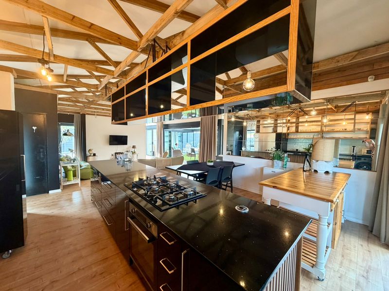 Spacious open-plan living area featuring exposed timber roof trusses, a modern kitchen island with gas hob, and contemporary finishes throughout.
