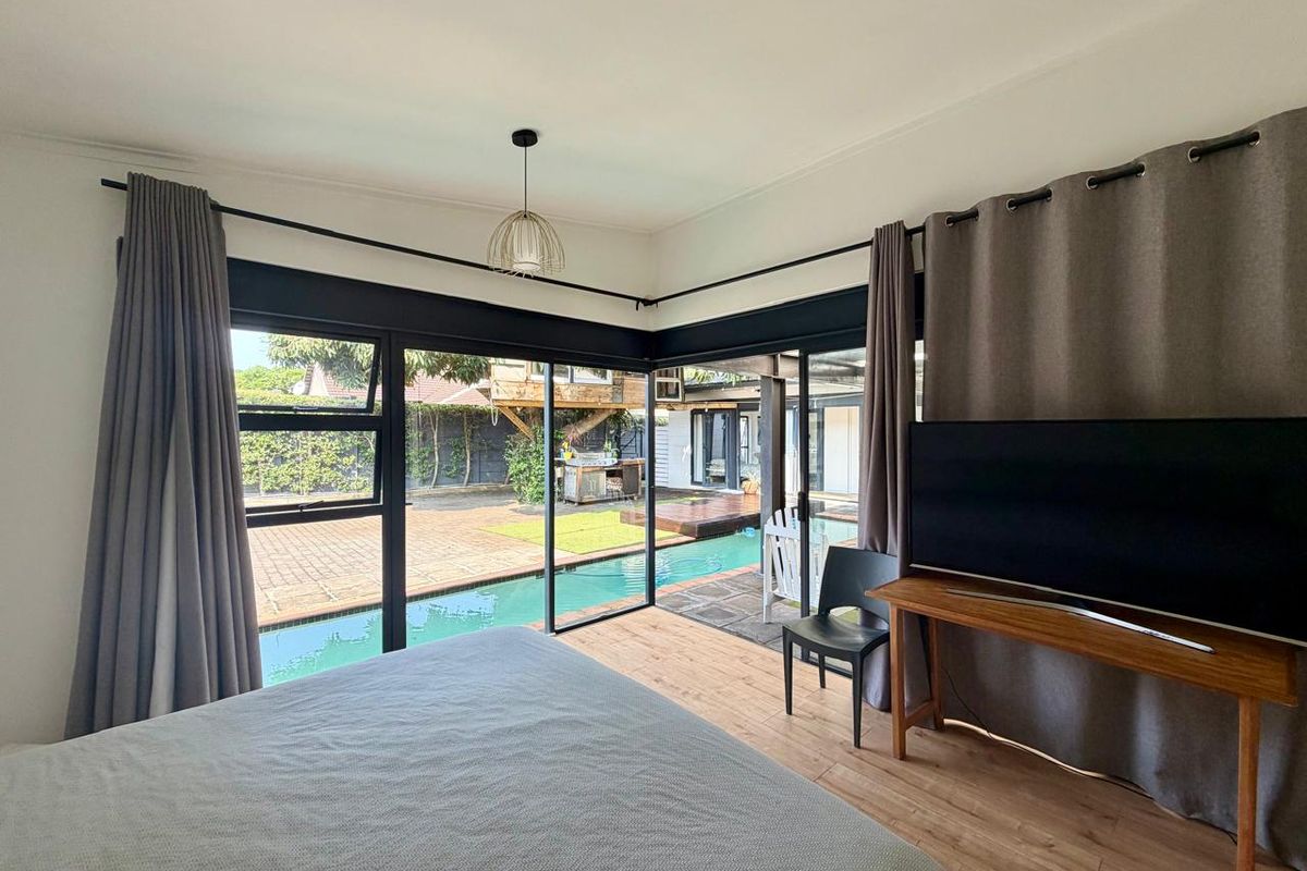 A bright bedroom featuring corner sliding glass doors that open directly onto a pool area, providing seamless indoor-outdoor flow and natural light.