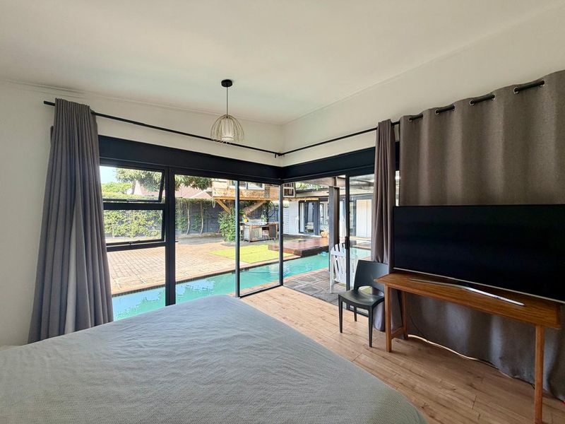 A bright bedroom featuring corner sliding glass doors that open directly onto a pool area, providing seamless indoor-outdoor flow and natural light.