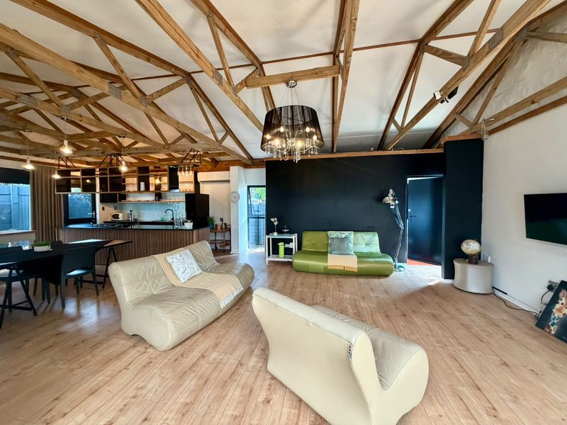 Spacious open-plan living area featuring exposed timber roof trusses, modern laminate flooring, and a contemporary kitchen with a central island.