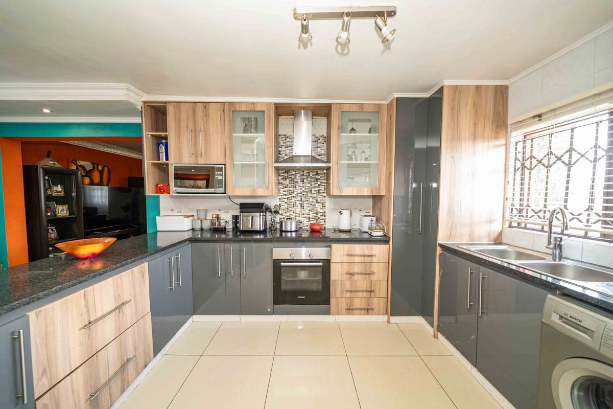 Modern kitchen featuring two-tone cabinetry, granite countertops, mosaic backsplash, built-in oven, extractor fan, and tiled flooring with ample storage space.