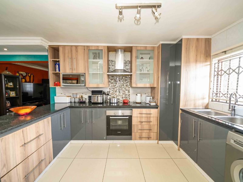 Modern kitchen featuring two-tone cabinetry, granite countertops, mosaic backsplash, built-in oven, extractor fan, and tiled flooring with ample storage space.