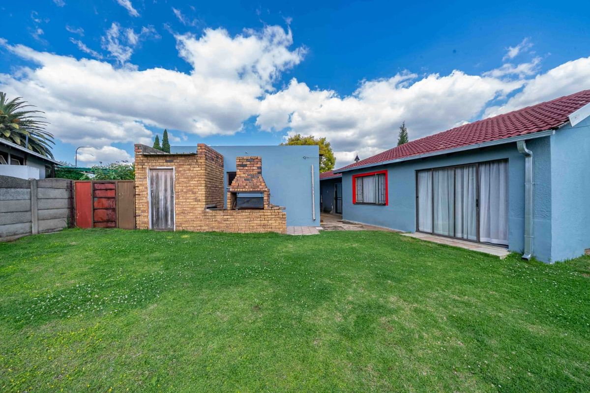 Rear exterior view featuring a spacious lawn, a built-in brick braai area, and sliding door access to the main house.