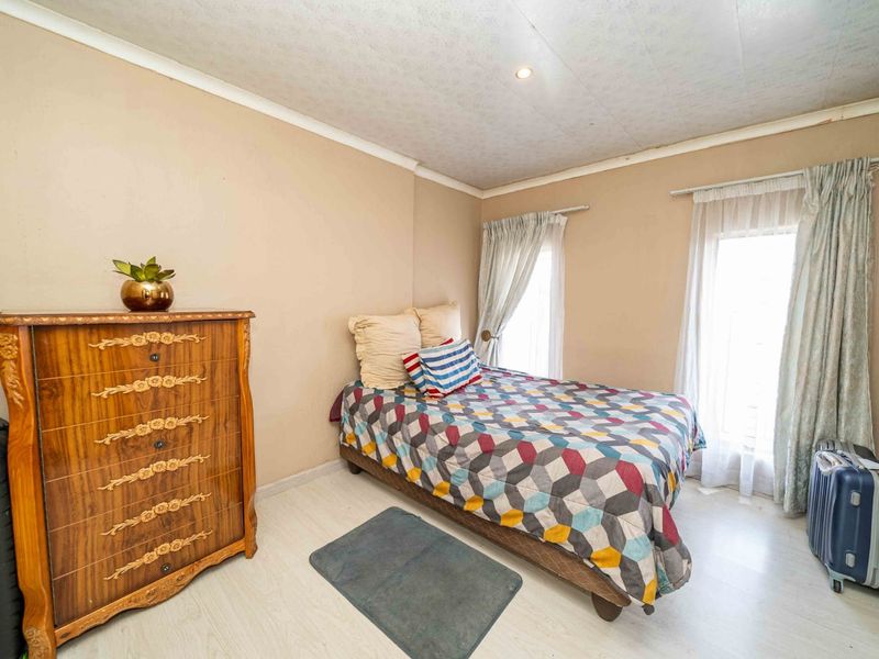 A bedroom featuring light-toned laminate flooring, neutral wall finishes, and dual windows with installed curtain rails.