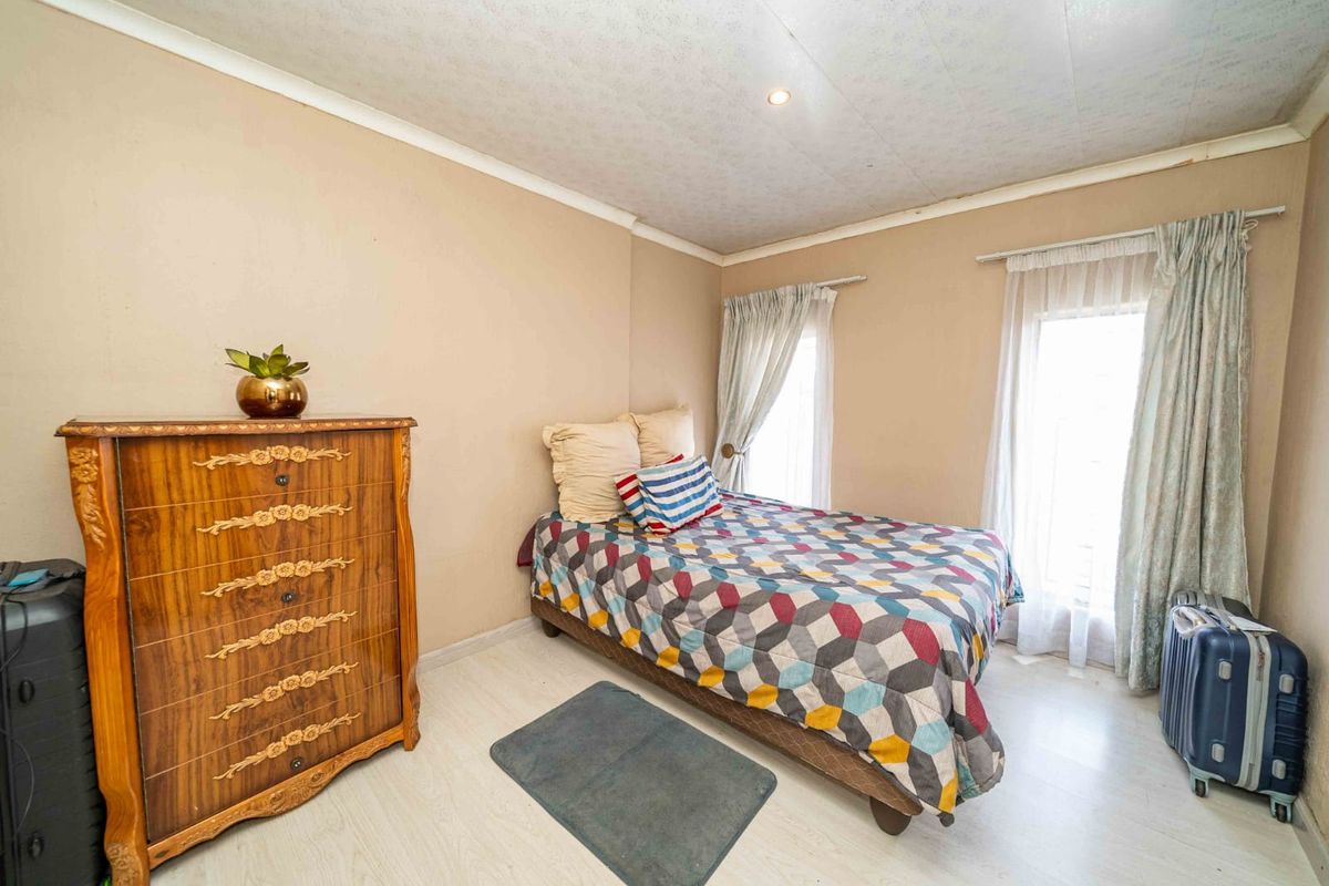 A bedroom featuring light-toned laminate flooring, neutral wall finishes, and dual windows with installed curtain rails.