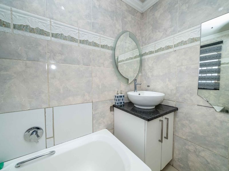 A functional bathroom featuring a vessel sink on a granite-topped vanity, a bathtub, and full-height wall tiling with decorative border accents.