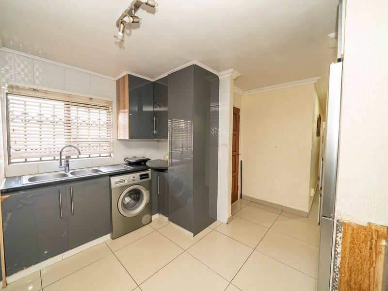 A functional kitchen featuring modern grey cabinetry, tiled flooring, a double sink, and an integrated washing machine with a convenient adjacent hallway.