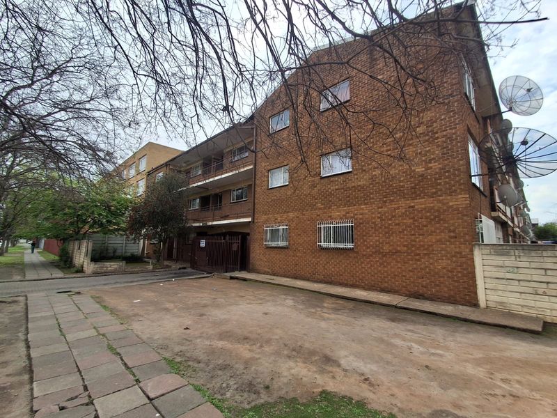 Exterior view of a multi-story face brick apartment building featuring security bars on lower windows and satellite dish installations.