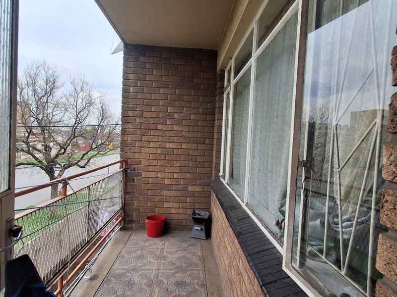 A covered balcony featuring brick walls, tiled flooring, and a metal balustrade, offering an outdoor space accessible from the main living area.