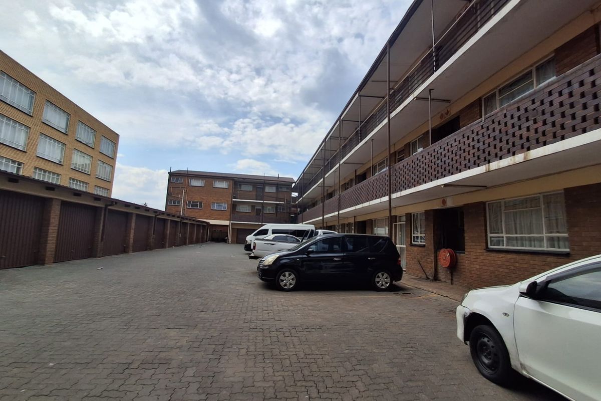 Exterior view of a multi-story apartment complex featuring brick facade, open balconies, and paved parking area with garage access.