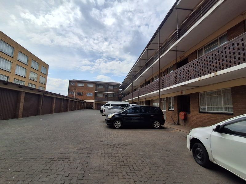 Exterior view of a multi-story apartment complex featuring brick facade, open balconies, and paved parking area with garage access.