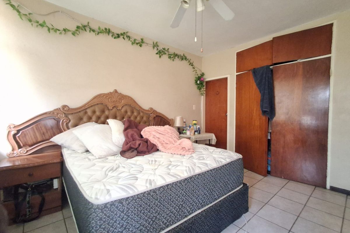 A bedroom featuring tiled flooring, a ceiling fan, and built-in wooden cupboards, offering a functional space with potential for modernization.