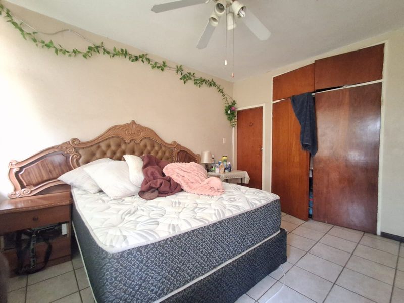 A bedroom featuring tiled flooring, a ceiling fan, and built-in wooden cupboards, offering a functional space with potential for modernization.
