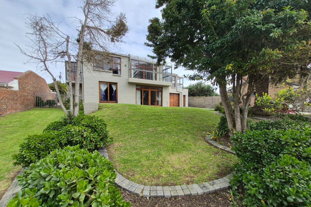 Rear view of a multi-story house featuring a landscaped lawn, established trees, and a balcony with glass balustrades overlooking the garden.
