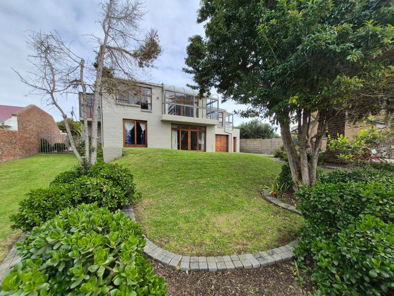 Rear view of a multi-story house featuring a landscaped lawn, established trees, and a balcony with glass balustrades overlooking the garden.