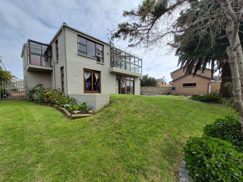 Rear view of a two-story house featuring an enclosed balcony, sliding glass doors, and a well-maintained garden area.