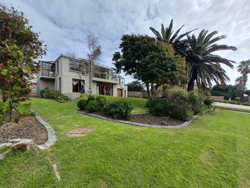 A view of the rear elevation of the house featuring a well-maintained lawn, landscaped garden beds, and an upper-level balcony.