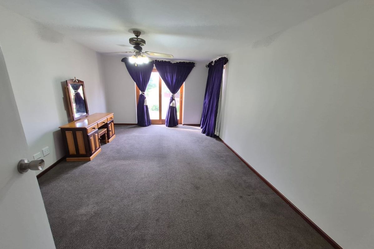 A spacious bedroom featuring neutral carpeting, a ceiling fan, and sliding glass doors that provide access to the outdoors.