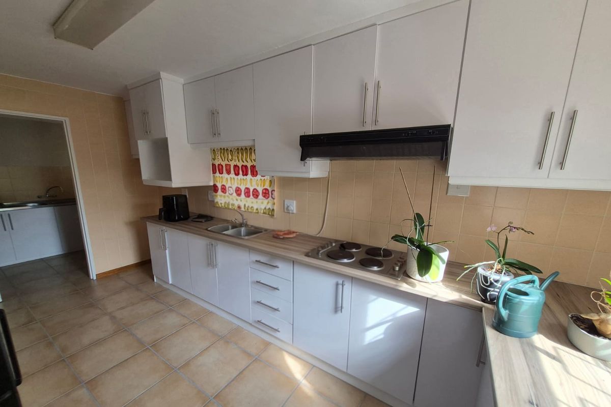 A functional kitchen featuring white cabinetry, a laminate countertop, integrated electric hob with extractor fan, and tiled flooring.