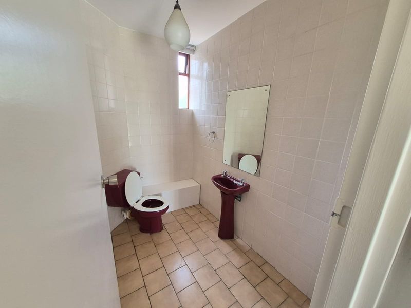A compact bathroom featuring dated burgundy sanitaryware, full-height wall tiling, and neutral floor tiles, offering potential for a modern renovation.