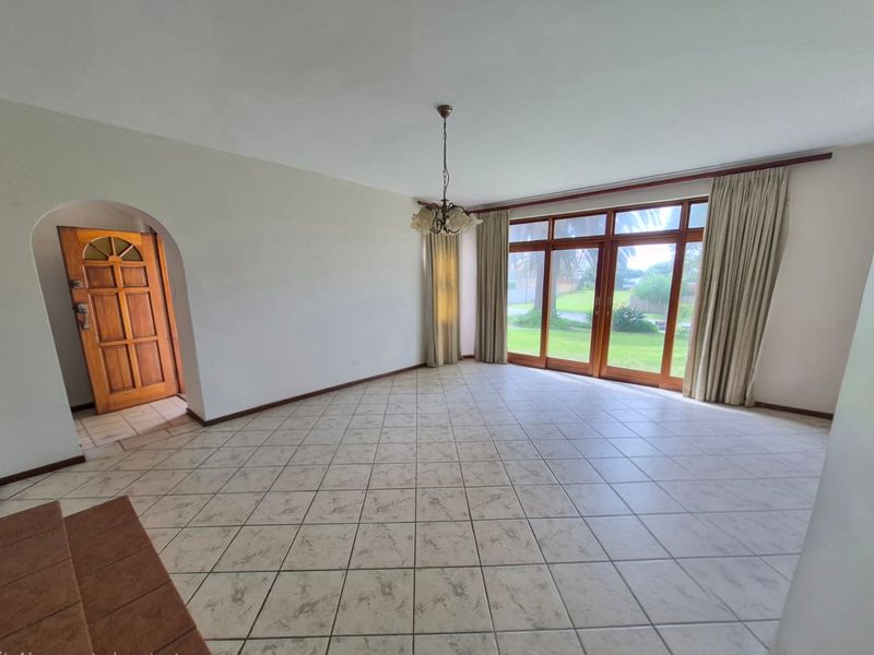 Spacious, light-filled living area featuring neutral tiled flooring, an arched entryway, and large timber-framed glass doors providing direct access to the garden.