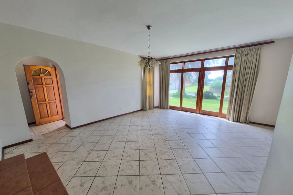 Spacious, light-filled living area featuring neutral tiled flooring, an arched entryway, and large timber-framed glass doors providing direct access to the garden.