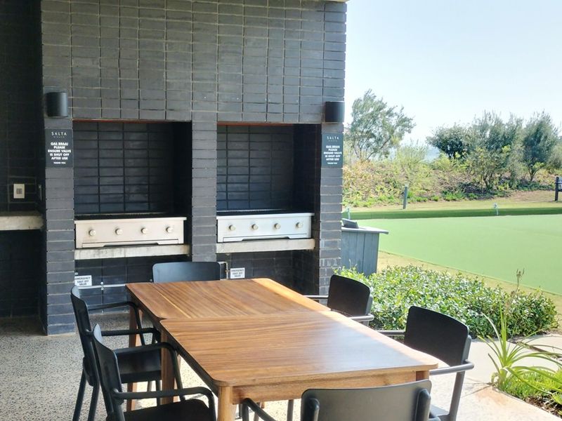A covered outdoor patio area featuring a dual built-in gas braai station with brick masonry, overlooking a manicured lawn.