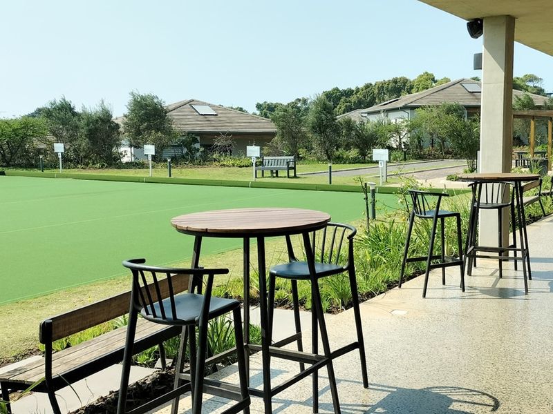 A spacious covered patio featuring durable terrazzo flooring and concrete columns, overlooking a well-maintained lawn and recreational area.