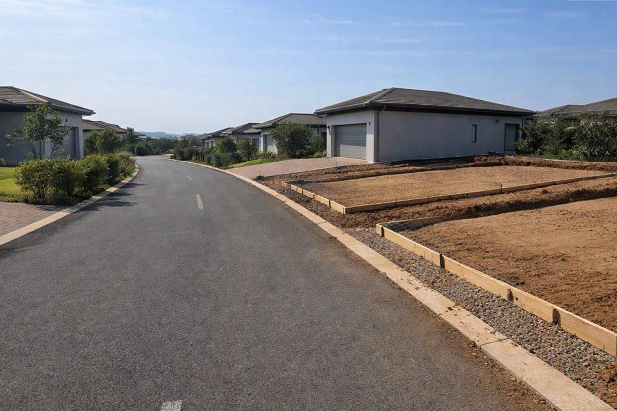 A street view of a residential estate featuring paved roads, established homes, and a prepared vacant plot ready for construction.