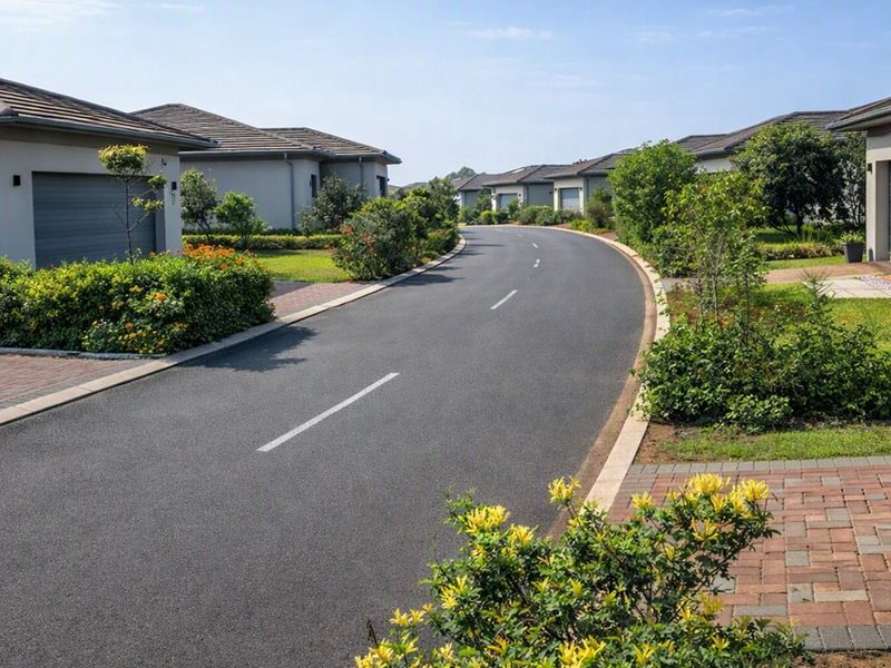 A well-maintained residential street view featuring paved driveways, landscaped garden beds, and modern housing units within a secure estate setting.