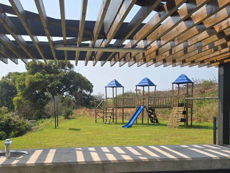 Covered outdoor patio area featuring a timber pergola, concrete countertop with sink, overlooking a landscaped garden with a children's playground.