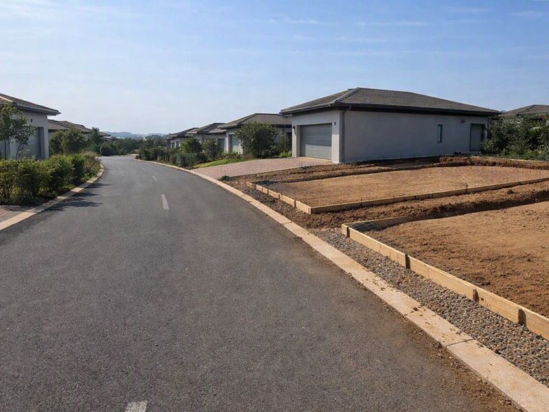 A street view of a residential estate featuring paved roads, established homes, and a prepared vacant plot ready for construction.