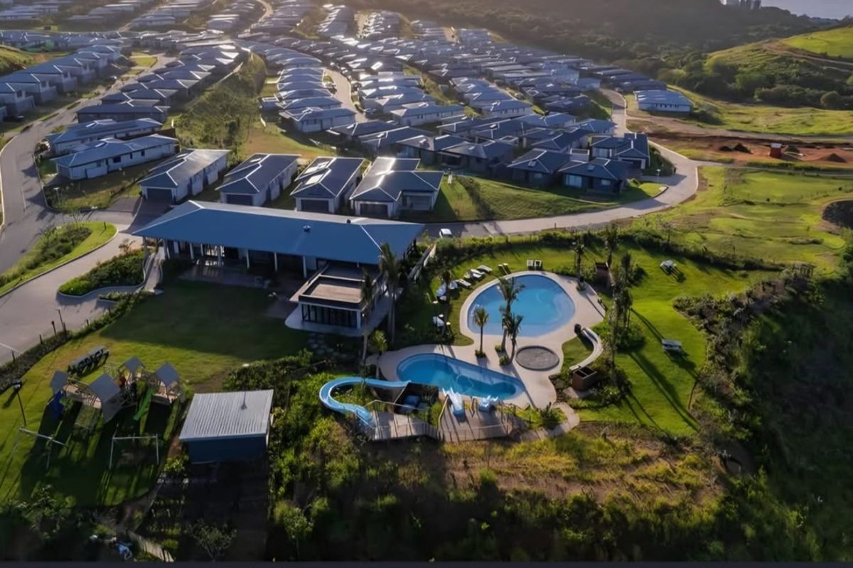 Aerial view of a residential estate featuring a clubhouse, swimming pools with water slides, and surrounding landscaped grounds.