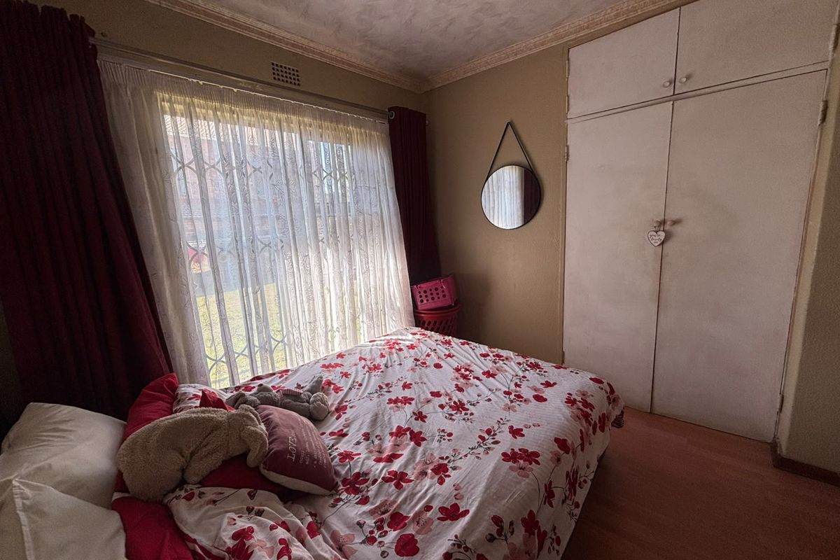 A bedroom featuring laminate flooring, built-in cupboards, and a security gate on the window, offering a functional space with potential for cosmetic updates.