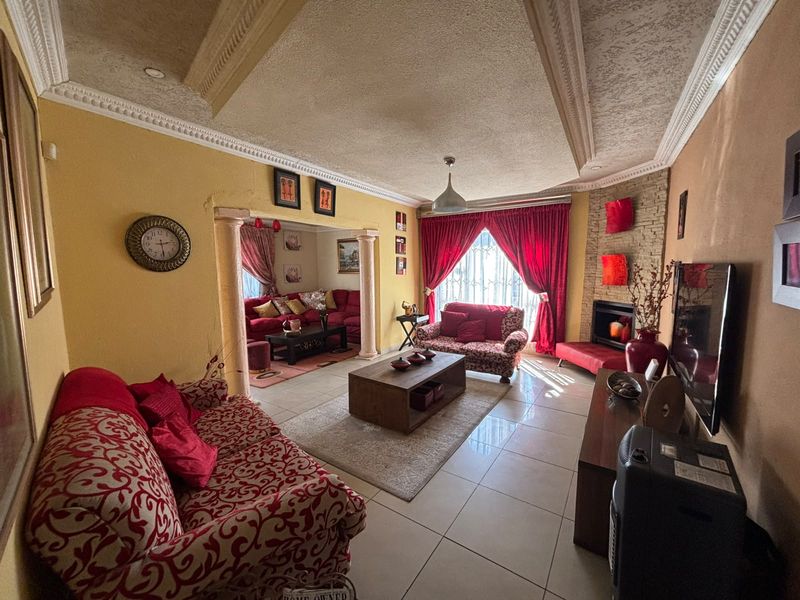 Spacious living room featuring a stone-clad fireplace, decorative columns, tiled flooring, and a detailed recessed ceiling with crown molding.