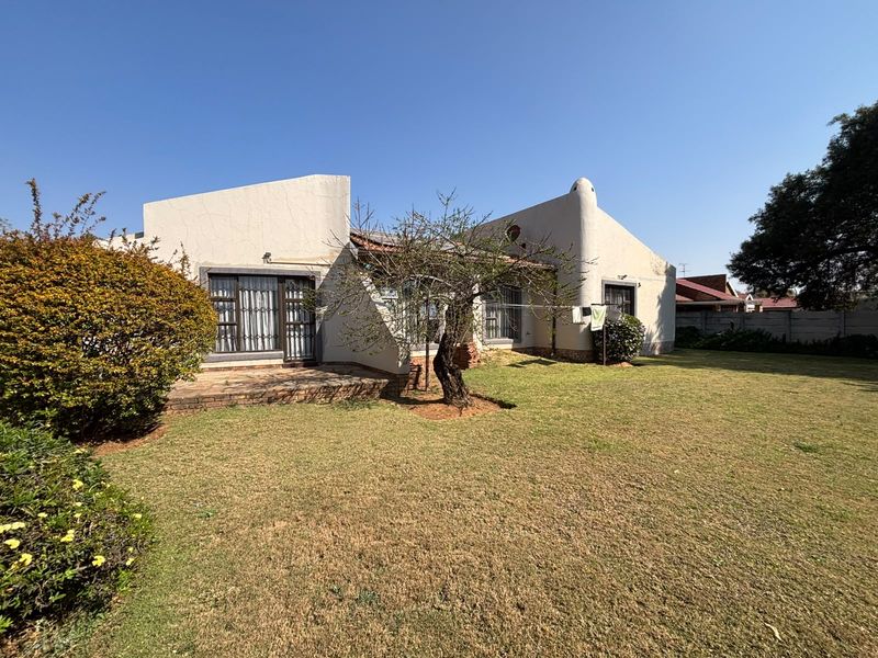 Rear view of the house featuring a paved patio area, established garden, and security-fitted sliding doors with visible exterior wall plaster cracking.