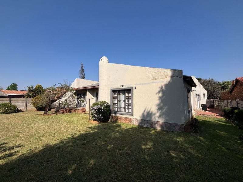 Rear view of the house showing the garden, plastered exterior walls with security bars, and a brick plinth foundation.