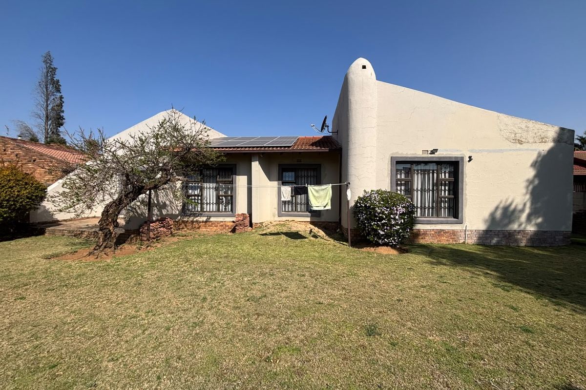Rear view of the house featuring a lawn, solar panels on the roof, and security bars on the windows.