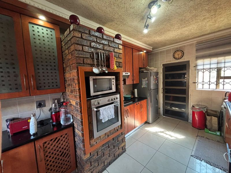 A functional kitchen featuring dark wood cabinetry, granite countertops, an exposed brick oven housing, and tiled flooring with a security door leading outside.