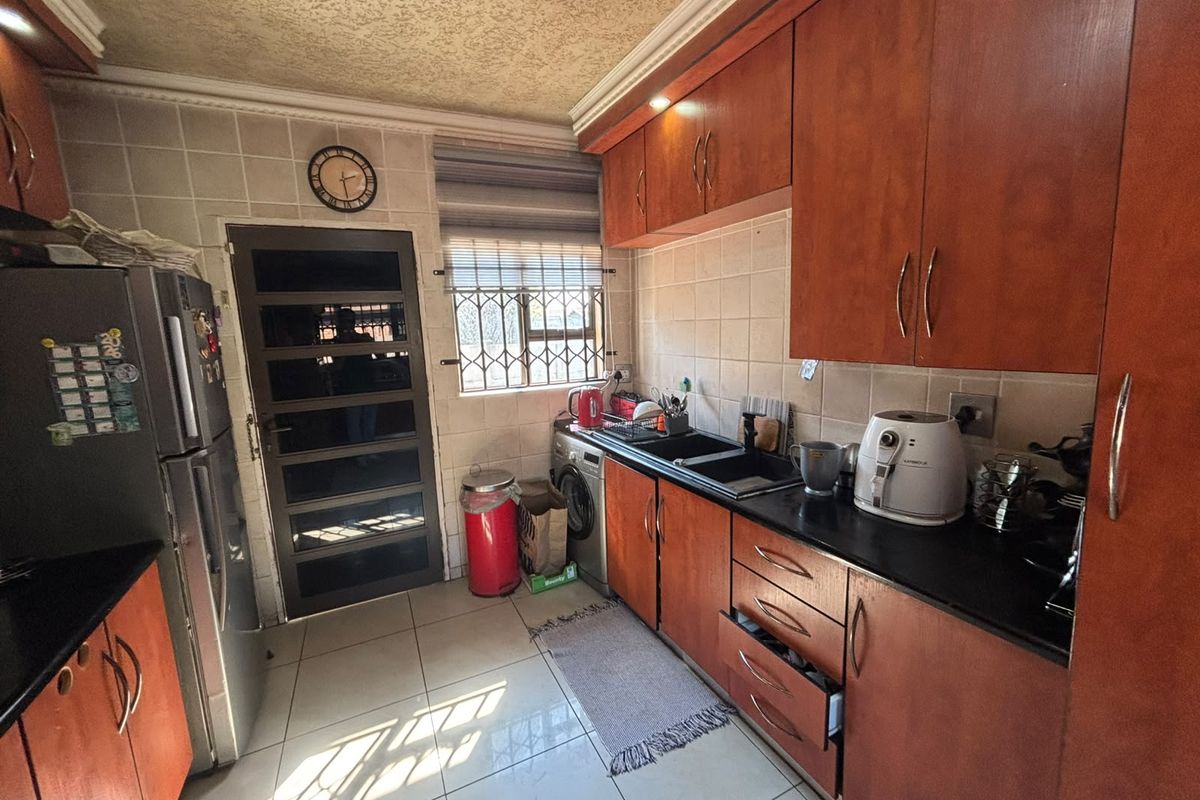 A functional kitchen featuring wooden cabinetry, black granite countertops, tiled backsplash, and secure access door with burglar bars.