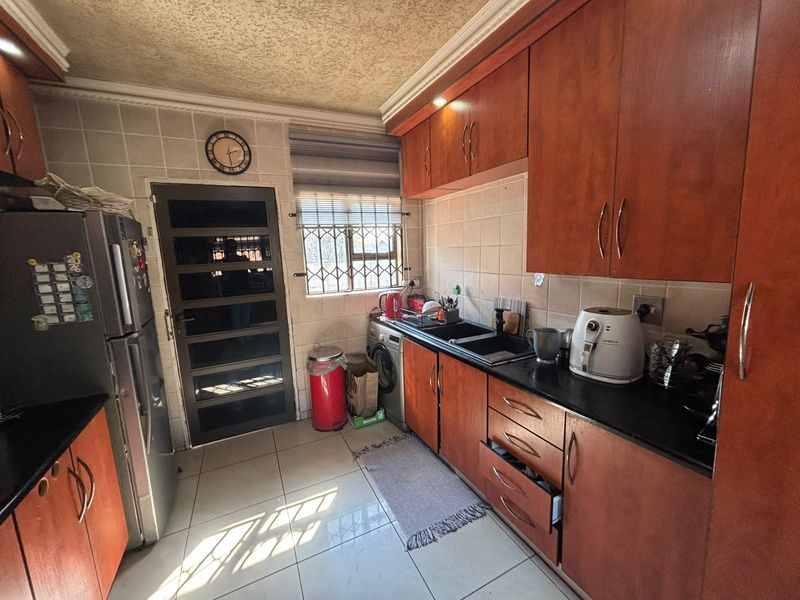 A functional kitchen featuring wooden cabinetry, black granite countertops, tiled backsplash, and secure access door with burglar bars.