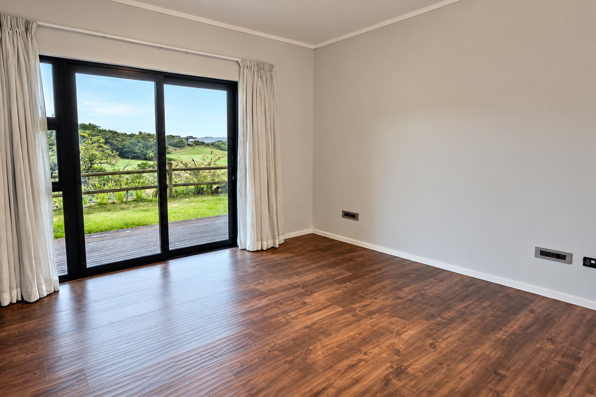 A bright, empty bedroom featuring modern laminate flooring, built-in cupboards, and a large sliding glass door providing access to an outdoor deck.