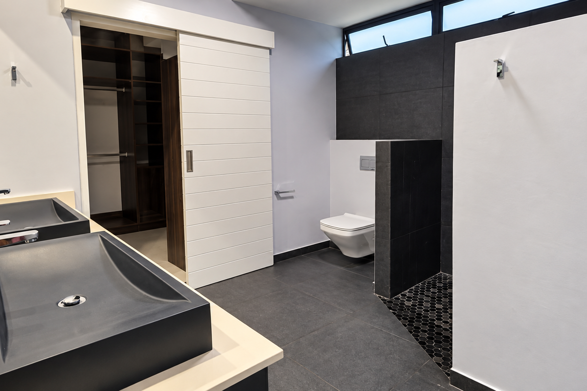 Modern bathroom featuring a double vanity with vessel sinks, wall-mounted toilet, dark floor tiling, and an integrated walk-in closet with sliding barn door access.