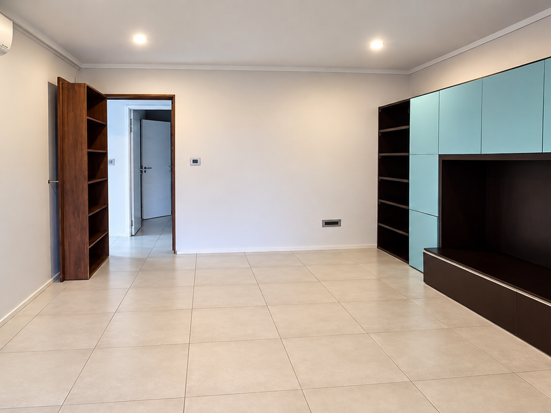 Spacious living area featuring neutral tiled flooring, recessed lighting, a wall-mounted air conditioning unit, and extensive built-in storage cabinetry.