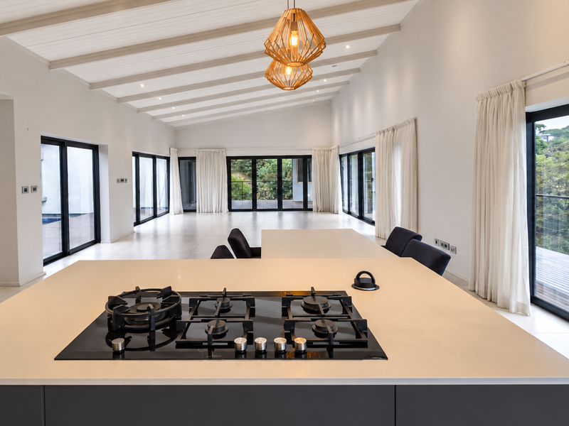 Spacious open-plan living area featuring a modern kitchen island with gas hob, vaulted ceilings with exposed beams, and large sliding doors opening to views.