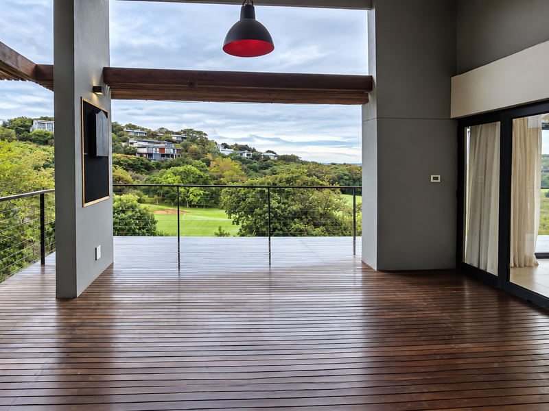 Spacious covered timber deck featuring a steel balustrade and expansive views over the surrounding landscape, accessible via large sliding glass doors.