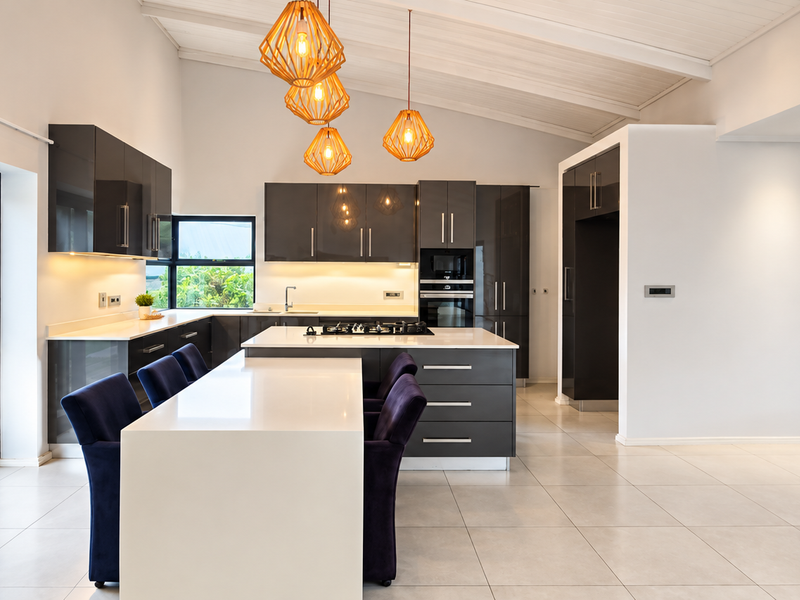 Modern open-plan kitchen featuring high-gloss cabinetry, stone countertops, integrated appliances, and a vaulted ceiling, seamlessly connecting to the living area and outdoor access.